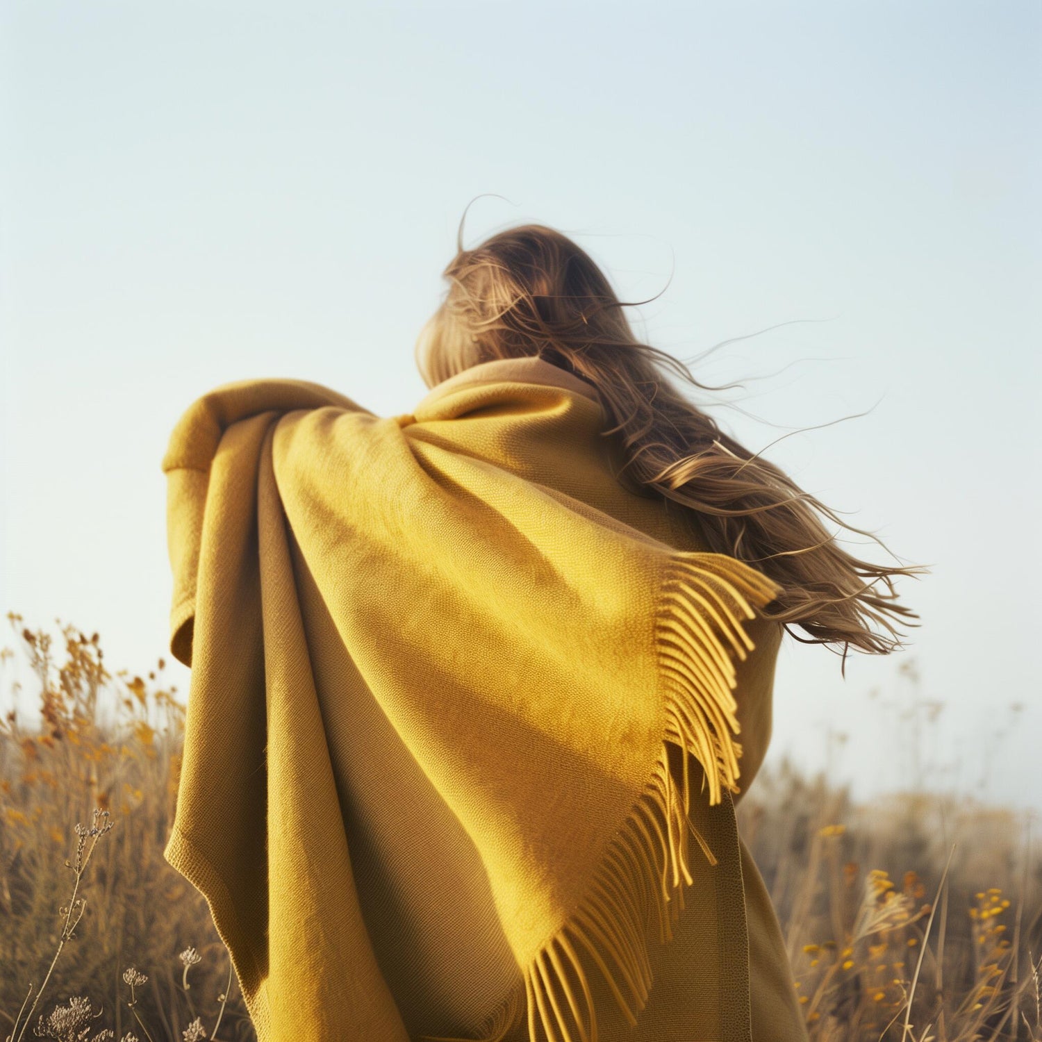 Textured natural bedding with decorative blanket in warm colours. Women wrapped her self cozy with a yellow blanket in a flower field setting, with wind blowing her hair, blanket and flowers back